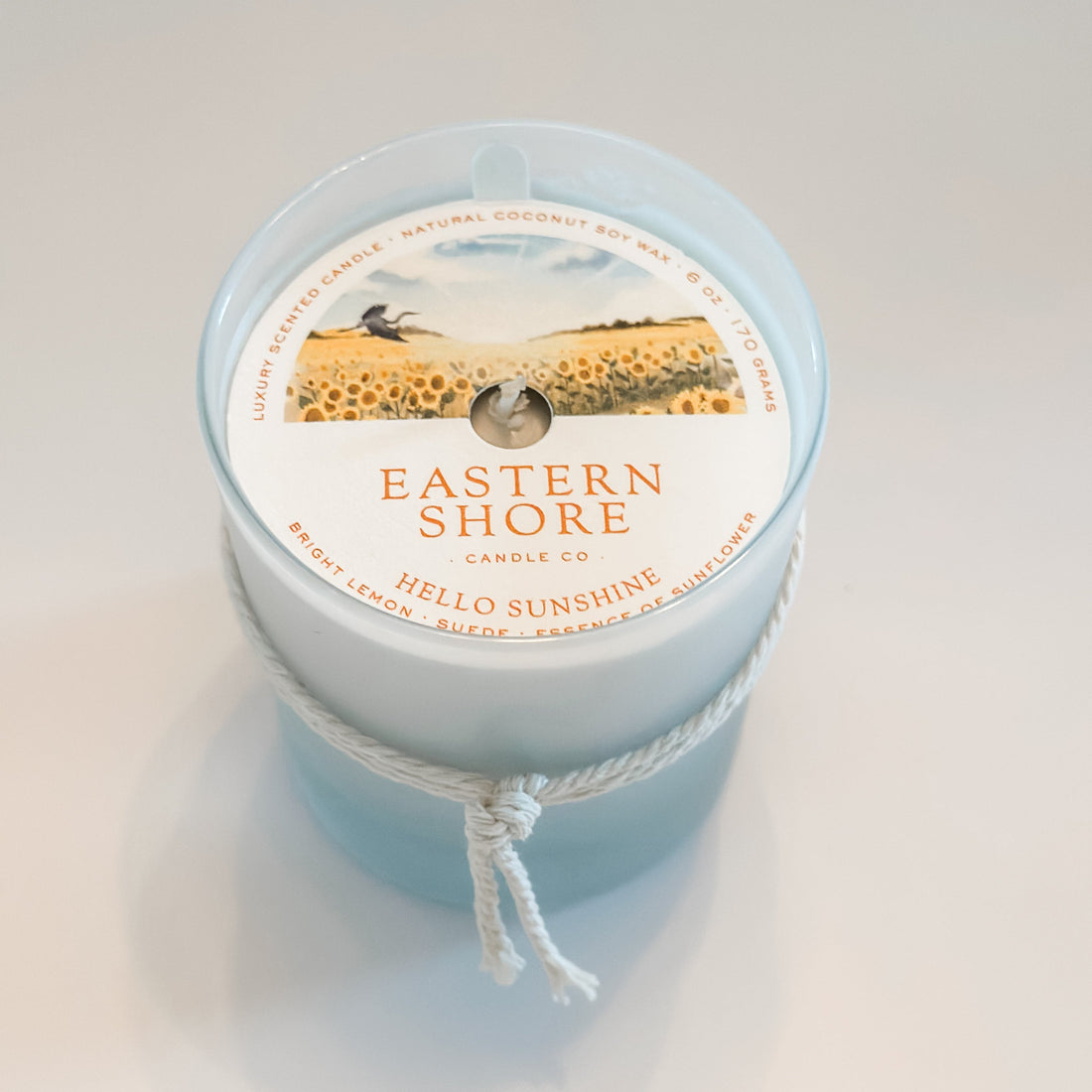 Eastern Shore Candle - Hello Sunshine scent in 6oz container against a white background.  Inside is a dust cover to protect the candle. 